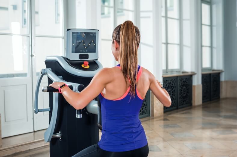 Eine junge Frau trainiert ihre Arme an einem Fitnessgerät.