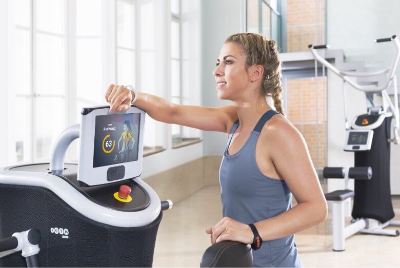 Junge Frau im Fitnessstudio leht an einem Traingsgerät.