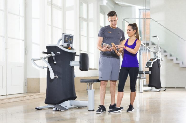 Zwei junge Menschen sehen sich ihre Trainingsergebnisse auf dem Handy und Tablet an.