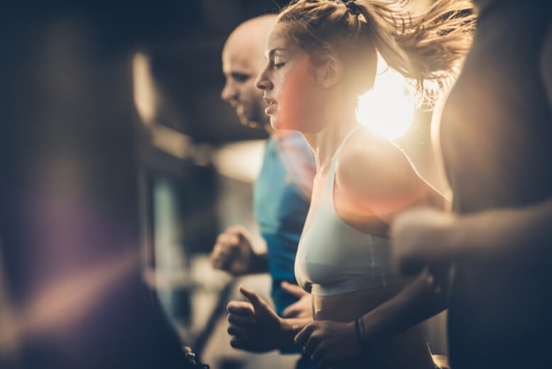 Im Fokus steht eine junge Frau, die konzentriert läuft, um sie herum trainieren weitere Menschen.