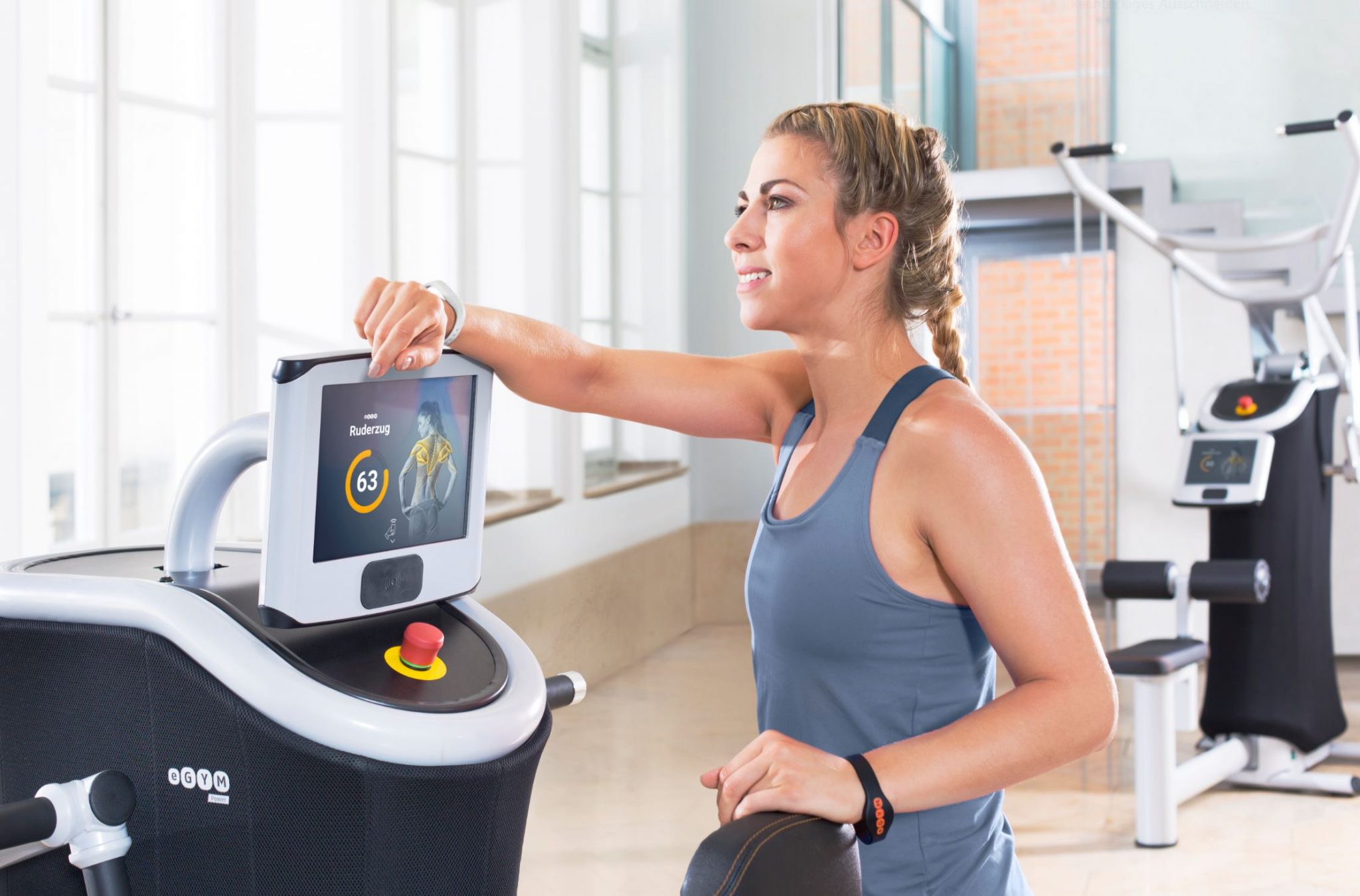 Ein Bild von einem eGym Gerät mit einer jungen Dame davor in grauem Shirt